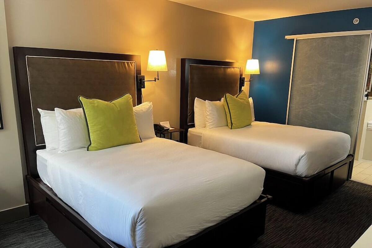 Two double beds with white linens and green pillows, bedside lamps, and a blue accent wall.