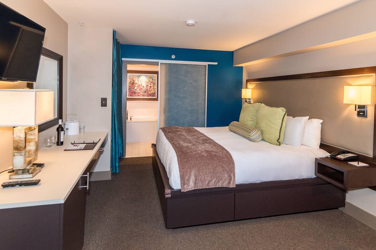 A hotel room with a bed, bedside table, lamp, and a desk with a telephone and a remote control.