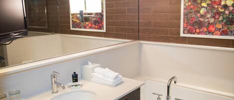 A modern bathroom with a large mirror, two sinks, a bathtub, and decorative wall art.