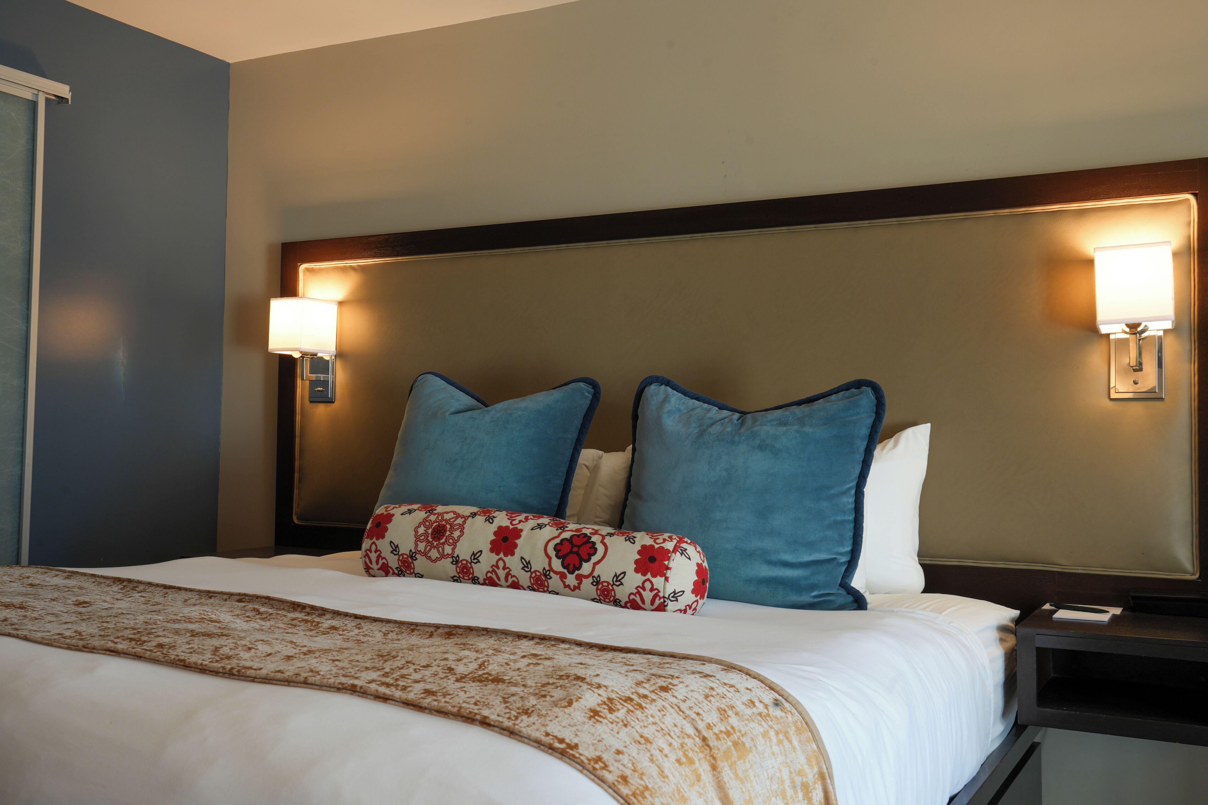 A hotel room with a large bed, two wall-mounted lamps, and a headboard.