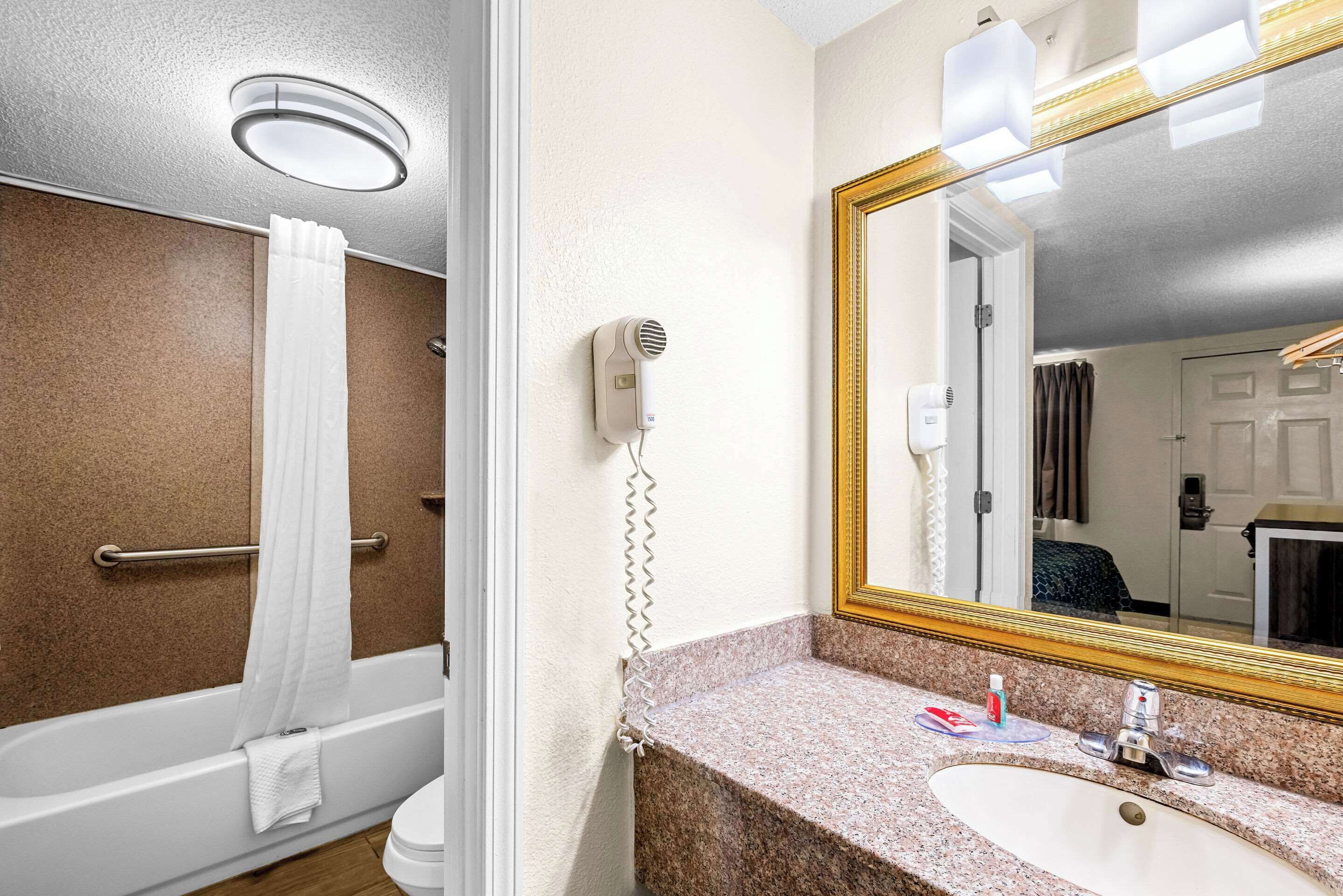 Un baño con bañera, lavabo, espejo y secador de pelo montado en la pared.