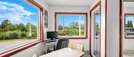 Una habitación con escritorio, silla y un ventanal que ofrece vistas a la vegetación y una carretera.