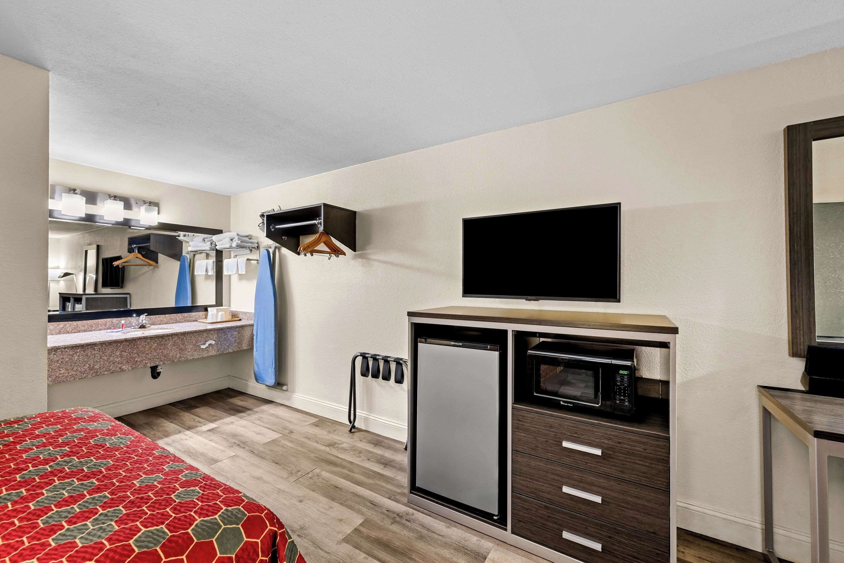 A compact hotel room with a bed, a kitchenette with a microwave, a small refrigerator, a TV, and a mirror.