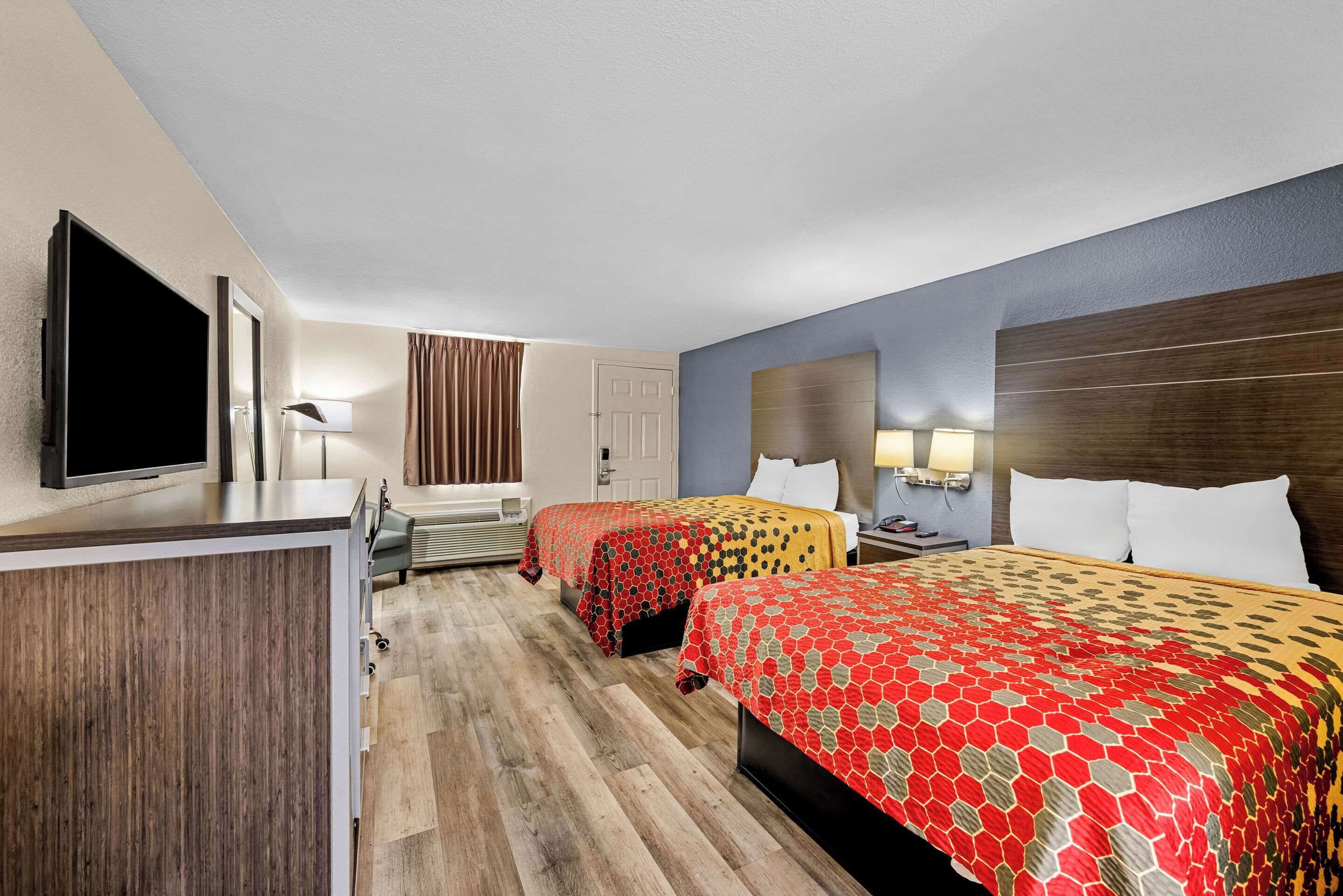A hotel room with two beds, a desk, a TV, and a window with curtains.
