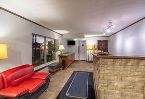 A compact living space with a red sofa, a stone accent wall, a TV mounted on the wall, and a small kitchen area with a counter and cabinets.