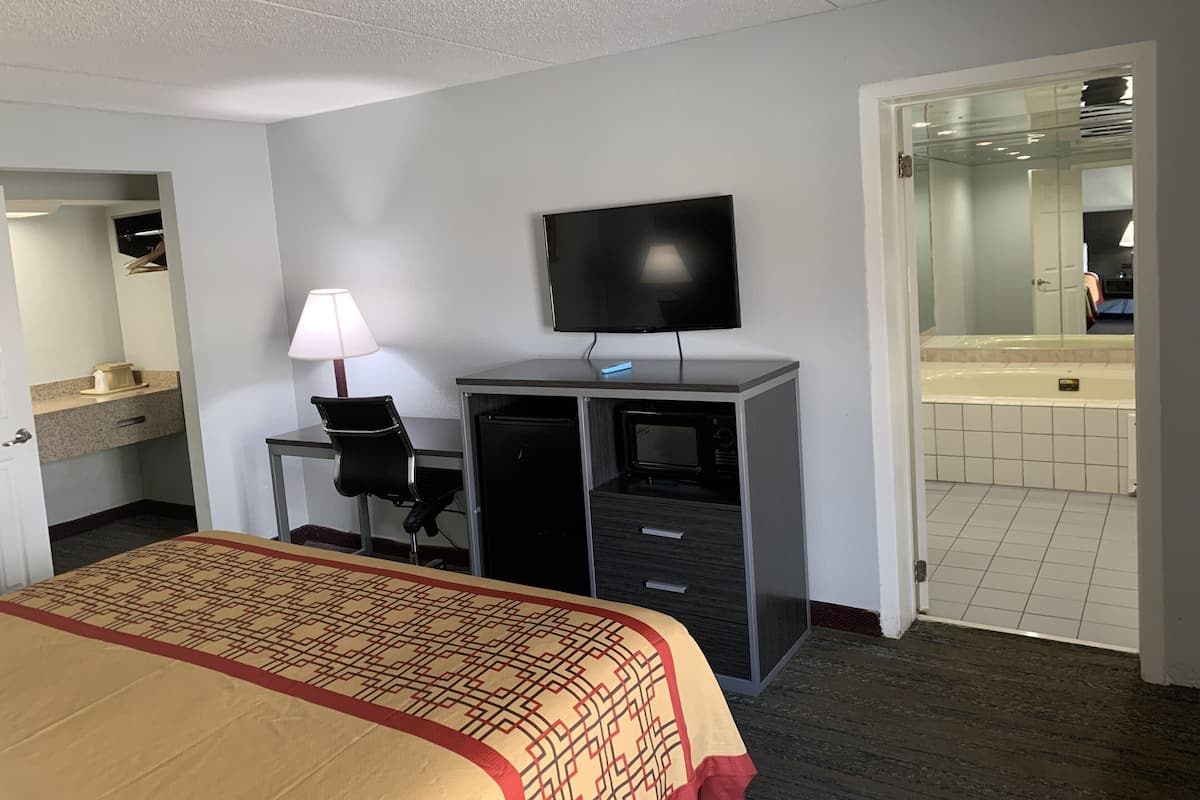 A hotel room with a bed, desk, TV, and a bathroom visible through an open door.