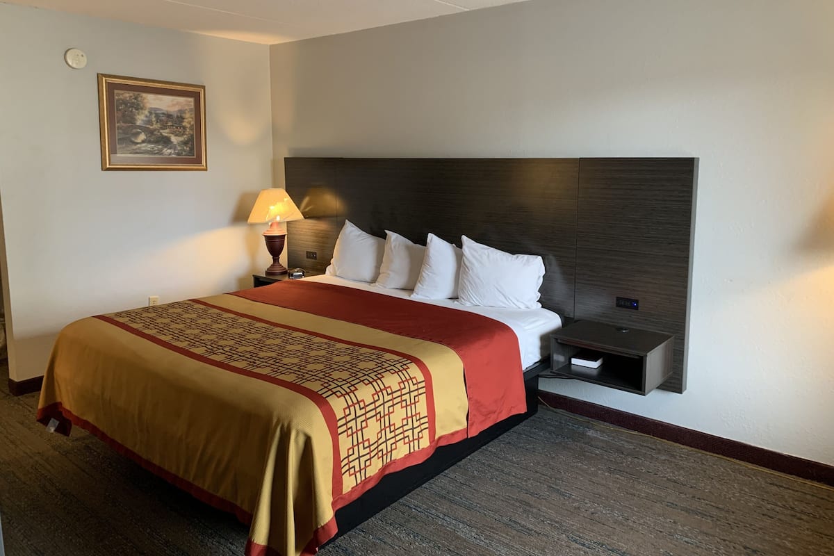 A hotel room with a large bed, a nightstand, a lamp, and a wall-mounted clock.