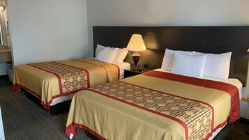 Habitación de hotel con dos camas, cada una con una colcha y almohadas estampadas, una mesita de noche con lámpara y un cabecero oscuro.