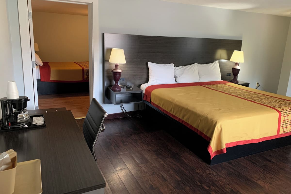 A hotel room with a large bed, two bedside tables with lamps, a desk with a coffee maker, and a chair.