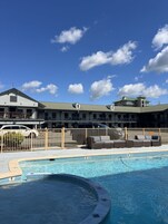 A hotel with a swimming pool, outdoor seating, and a fenced parking area.