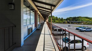 A covered outdoor area with a concrete floor, metal railings, and a view of parked cars and greenery in the background. - Edyn Hotel By Townhouse Wytheville US 52 (Wytheville)