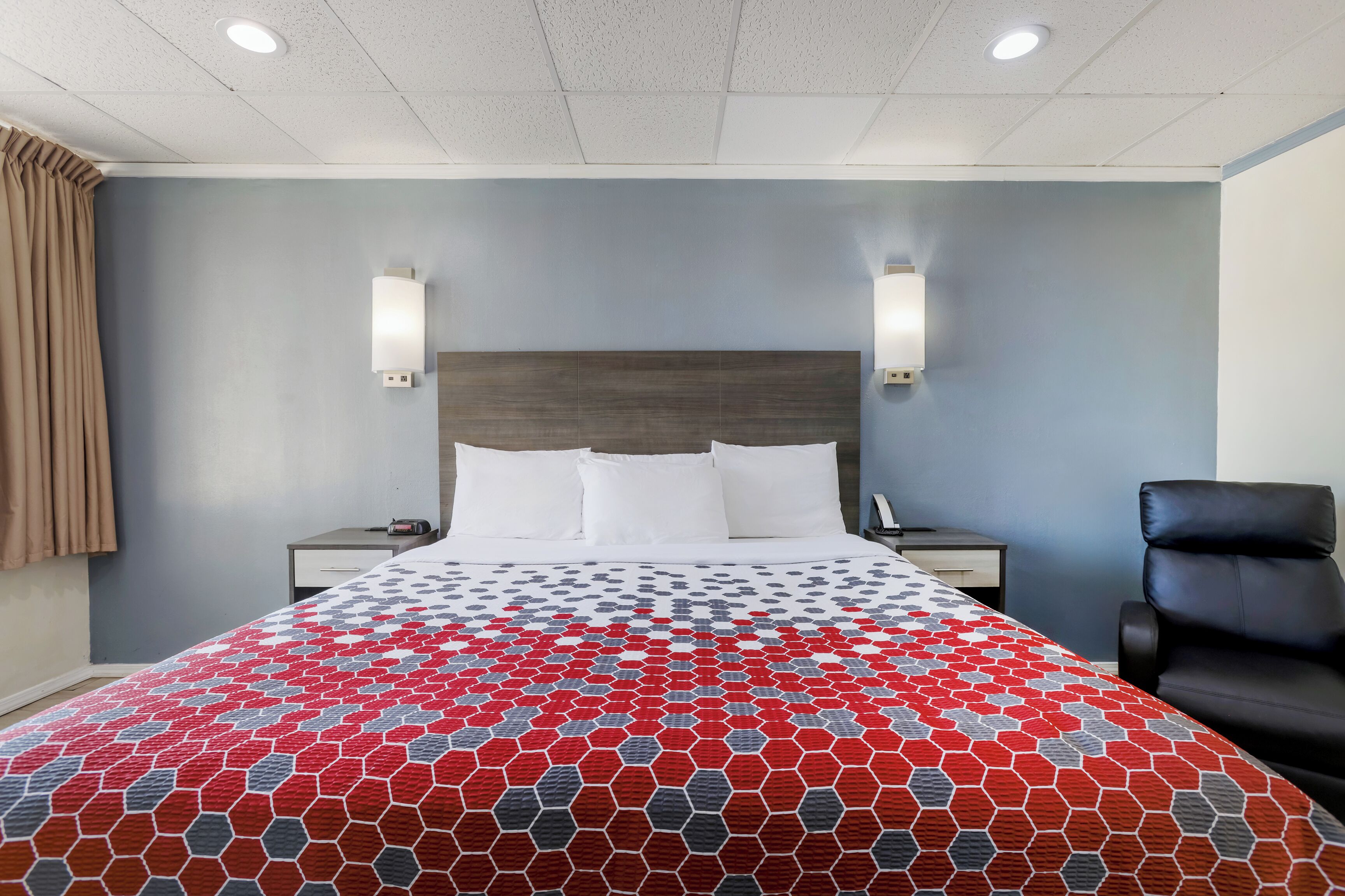 Une chambre d’hôtel avec un grand lit, deux tables de chevet, un fauteuil en cuir noir et un mur bleu clair.