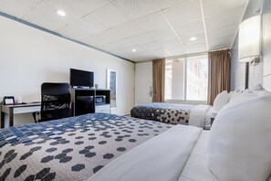 A hotel room with two beds, a desk with a computer, a TV, and a window with curtains.