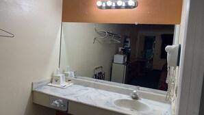 A bathroom with a large mirror, a sink, a vanity, a hairdryer, and a towel rack.