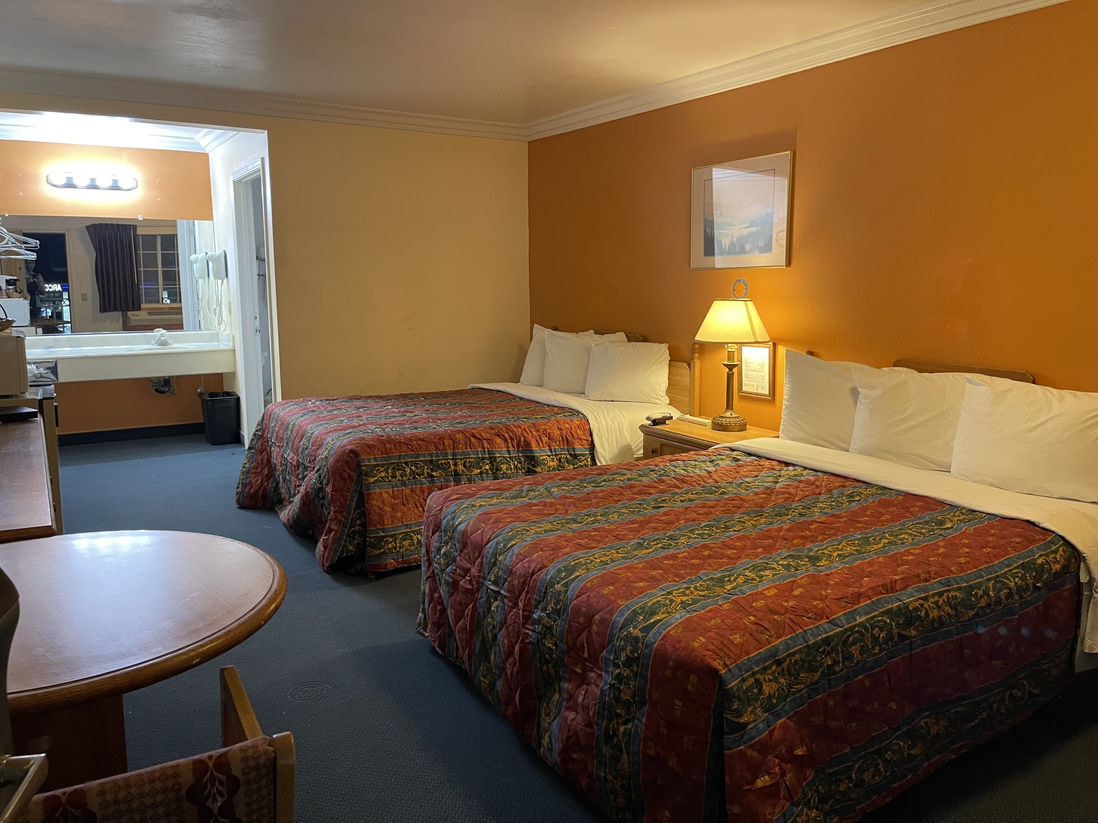 A hotel room with two beds, a desk, a chair, a lamp, and a picture on the wall.