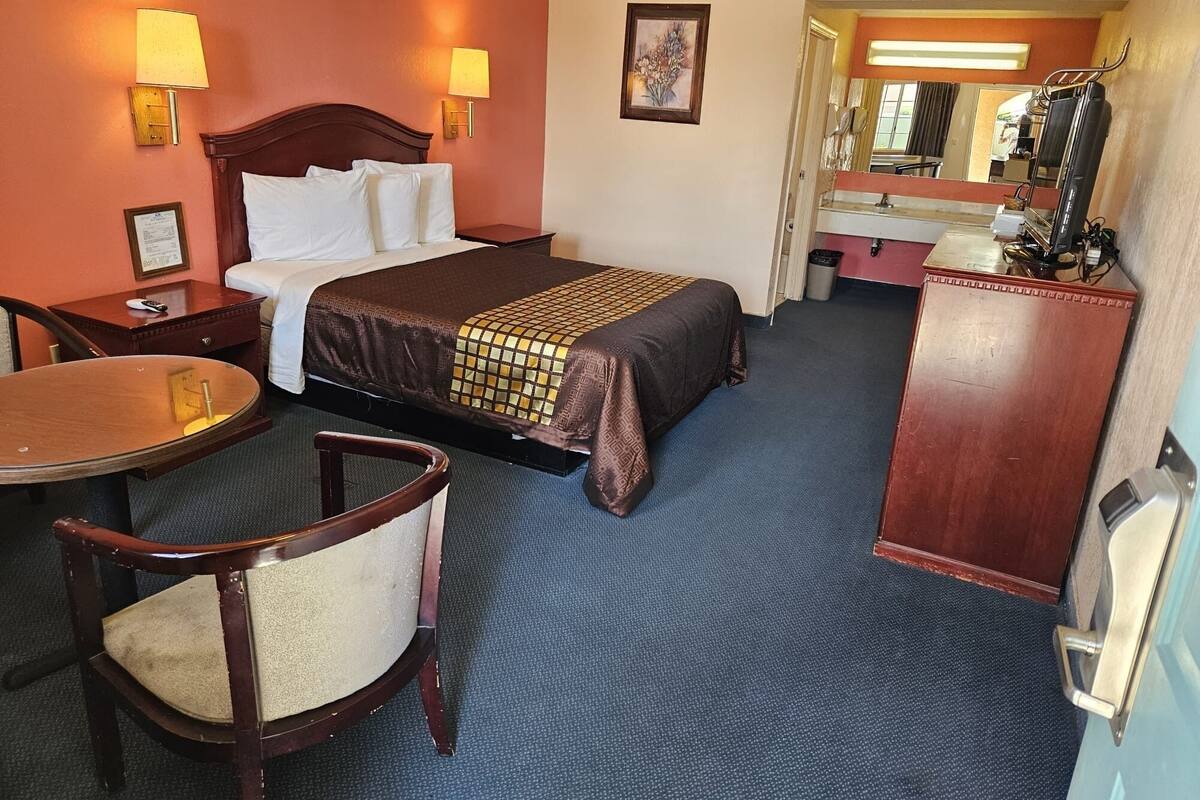 A hotel room with a bed, a desk, a chair, a dresser, and a mirror.