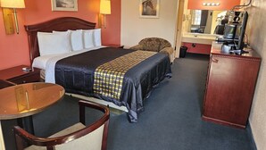 A hotel room with a large bed, a desk, a chair, a dresser, and a mirror.