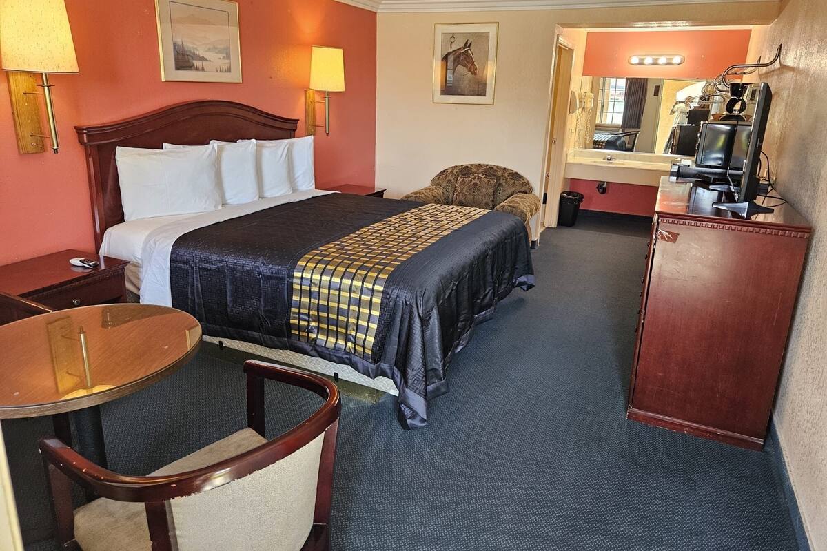 A hotel room with a large bed, a desk, a chair, a dresser, and a mirror.