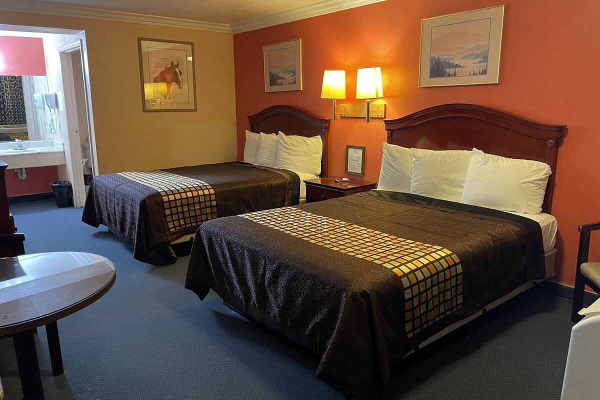 A hotel room with two beds, a desk, a chair, and a bathroom visible through an open door.