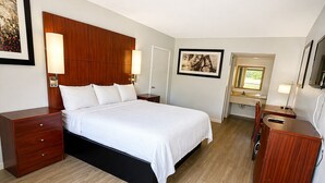 A hotel room with a bed, bedside tables, a desk, a chair, and a wardrobe. - American Inn and Suites (Jasper)