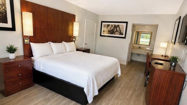 A bedroom with a bed, bedside tables, a dresser, a desk, and a chair. - American Inn and Suites (Jasper)