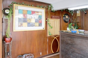 A reception area with a wooden wall, a framed artwork, a welcome sign, and a fire alarm. - American Inn and Suites (Jasper)