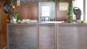 A reception desk with a wooden finish, a fire alarm, and a window with a view of the outside. - American Inn and Suites (Jasper)