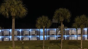 A motel with multiple rooms, each with a door and a window. There are palm trees in front of the building. - American Inn and Suites (Jasper)
