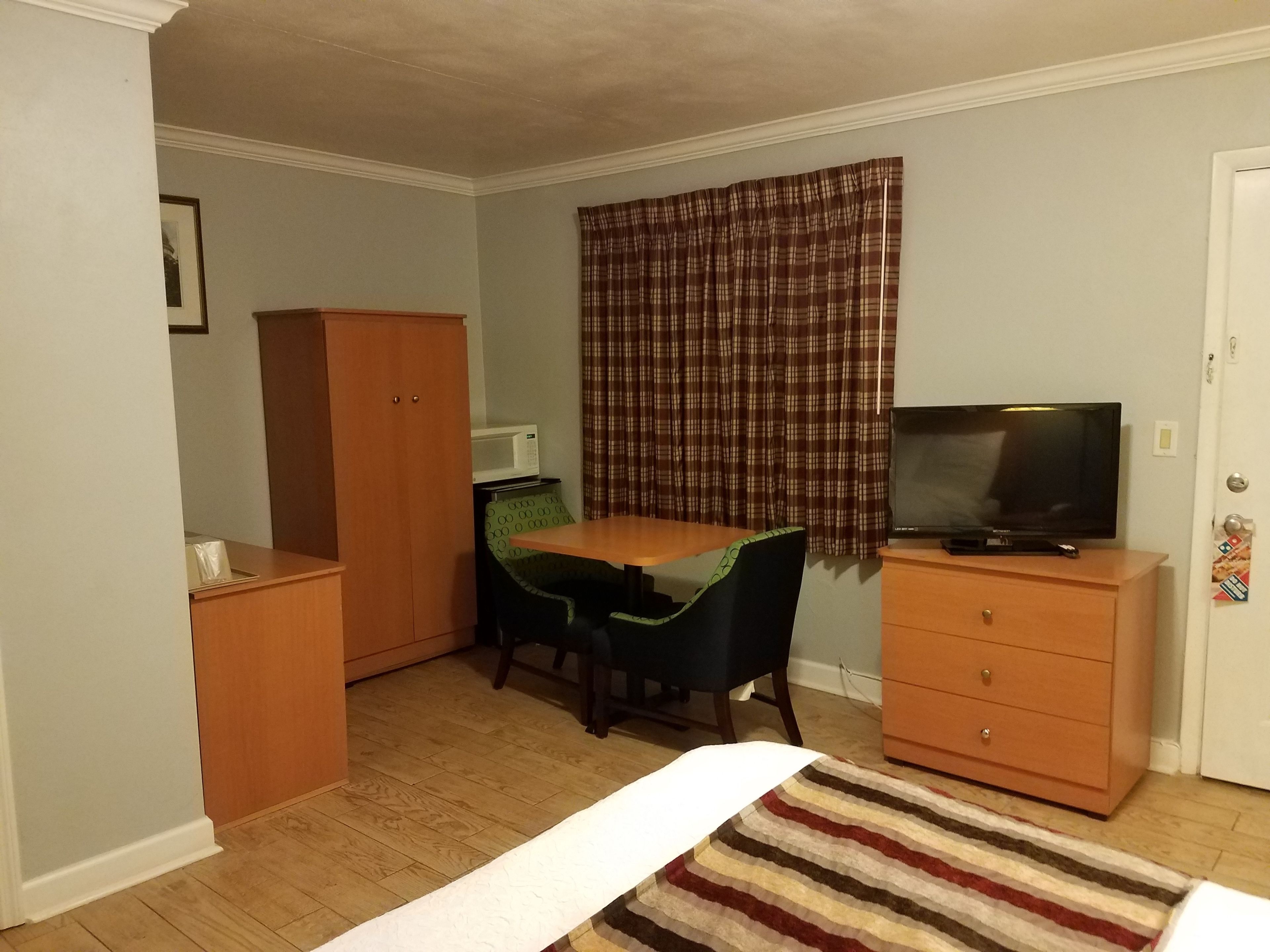 A compact room with a bed, a desk with a chair, a television, a wardrobe, and a microwave.