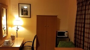 A compact hotel room with a desk, chair, wardrobe, and a bed with a green patterned bedspread.