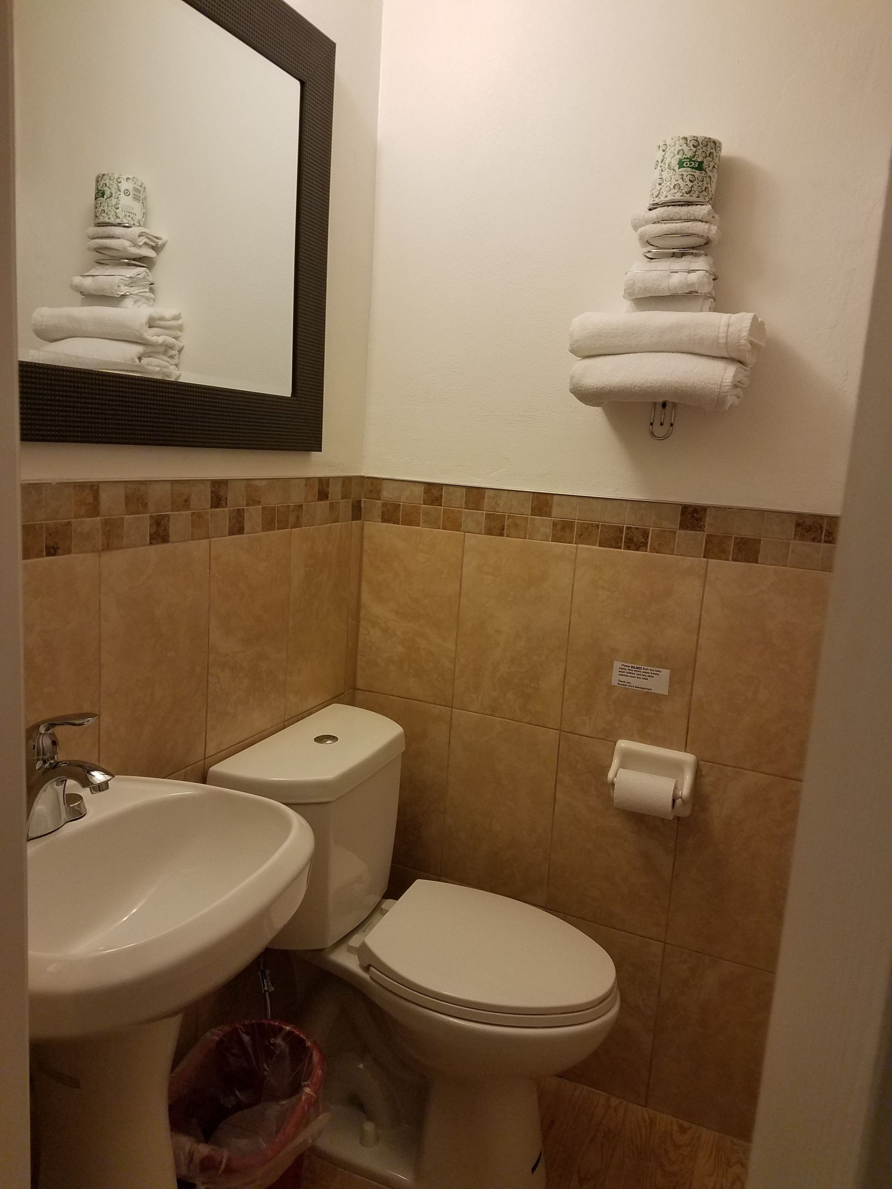 Un baño con un lavamanos, dos inodoros, un perchero para toallas y un espejo.