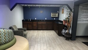Eine moderne Hotelhalle mit Küchenzeile, Holzschränken und einer Sitzecke mit Sofa und Sesseln.