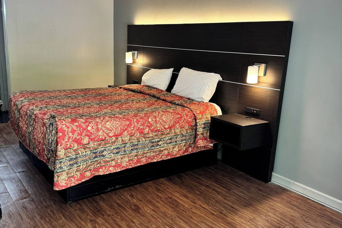 A neatly made bed with a patterned bedspread, two bedside tables with lamps, and a wooden floor.
