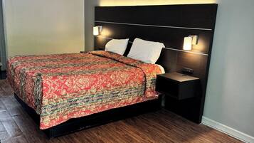 A neatly made bed with a patterned bedspread, two bedside tables with lamps, and a wooden floor.