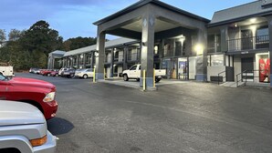 Ein mehrstöckiges Motel mit überdachtem Parkplatz, mehreren Zimmern und einer Coca-Cola-Getränkeautomaten.
