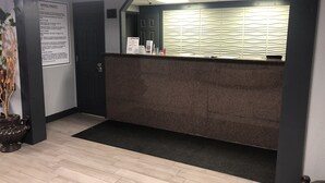 Ein Hotel-Rezeptionsbereich mit dunklem Empfangstresen, einem Aushang mit den Hotelrichtlinien und einer Tür zu den Zimmern.
