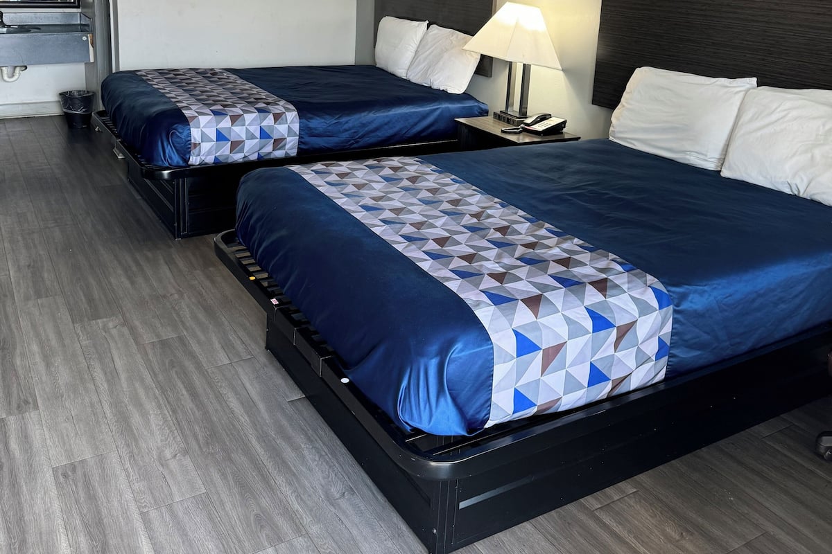 A hotel room with two beds, a desk, and a mirror.