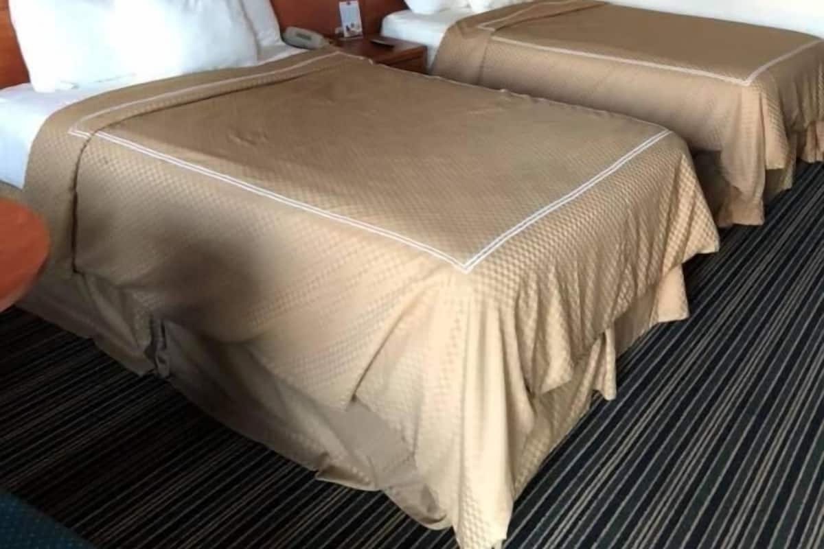 A hotel room with two beds, a nightstand, a lamp, and a framed picture on the wall.