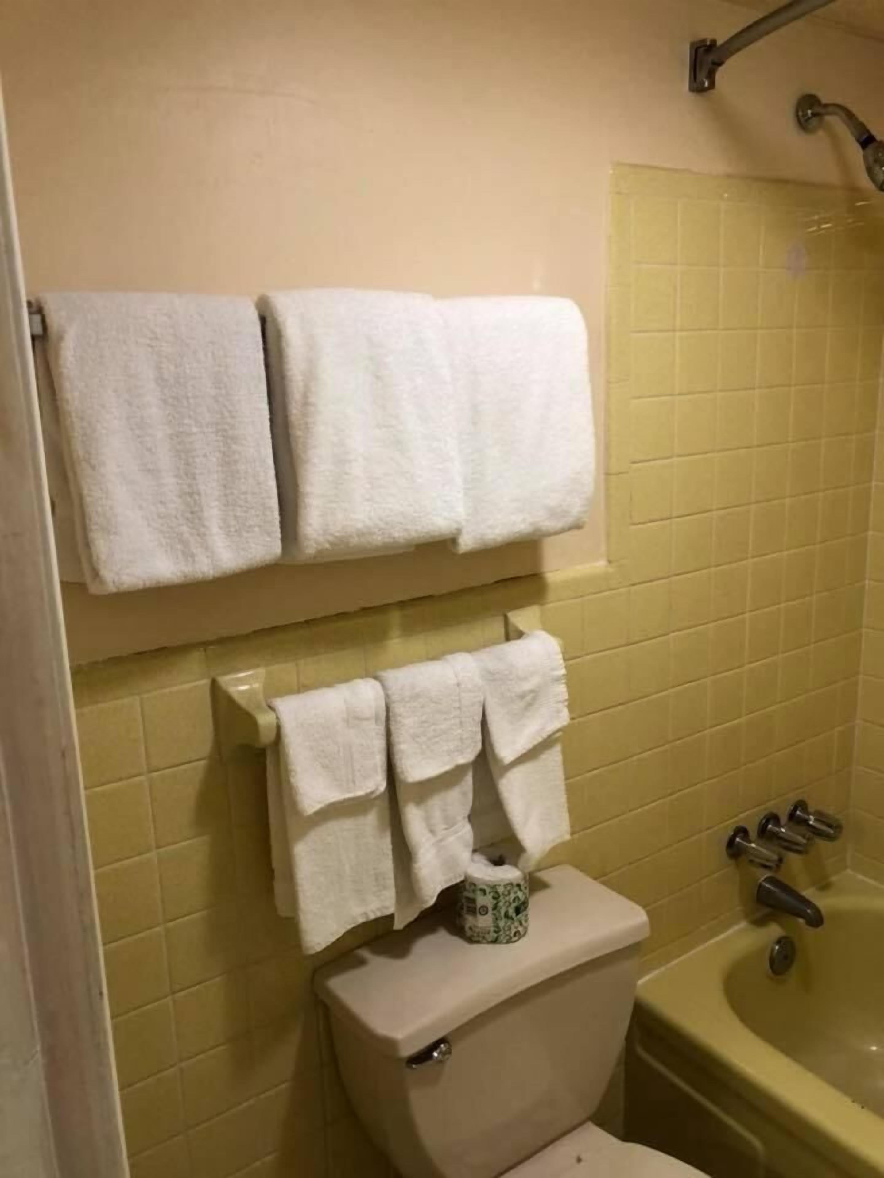 Ein Badezimmer mit gelb gefliesten Wänden, einer Toilette, einer Badewanne und zwei Handtuchhaltern mit weißen Handtüchern.
