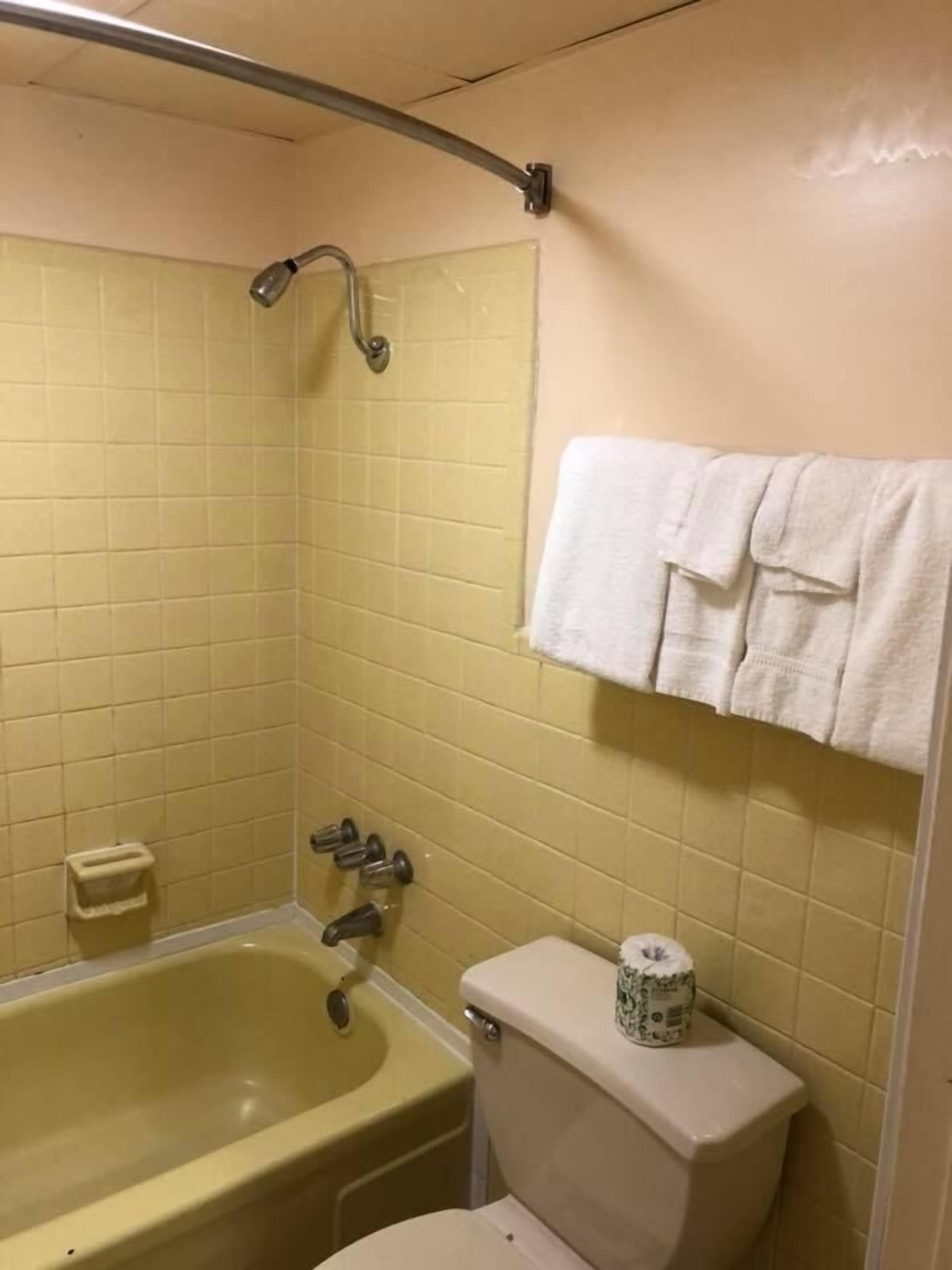 Casa de banho com azulejos amarelos, uma banheira, sanita e um porta-toalhas com toalhas.