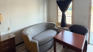Une pièce comprenant un canapé, une table en bois, une lampe et une fenêtre avec des rideaux.