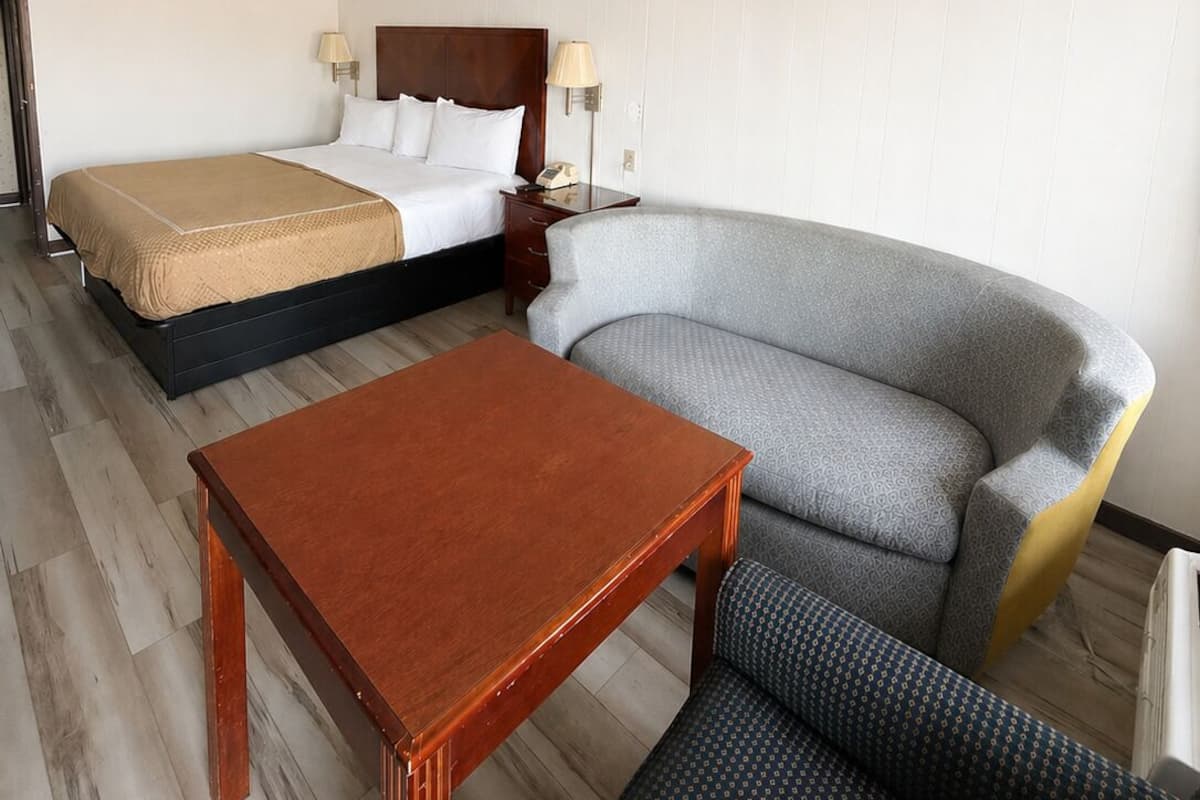A hotel room with a bed, a sofa, a table, and a lamp.