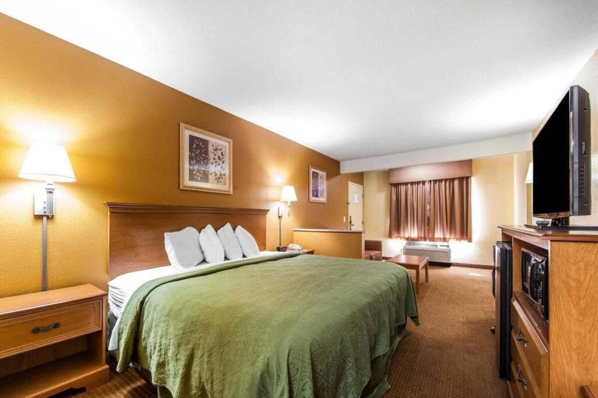 Une chambre d’hôtel avec un lit, des lampes de chevet, un bureau, une télévision et une fenêtre avec des rideaux.