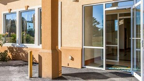 A building with large glass doors and windows, a concrete pillar, and a small outdoor area with a mat and plants. - Quality Inn & Suites Cartersville North (White)