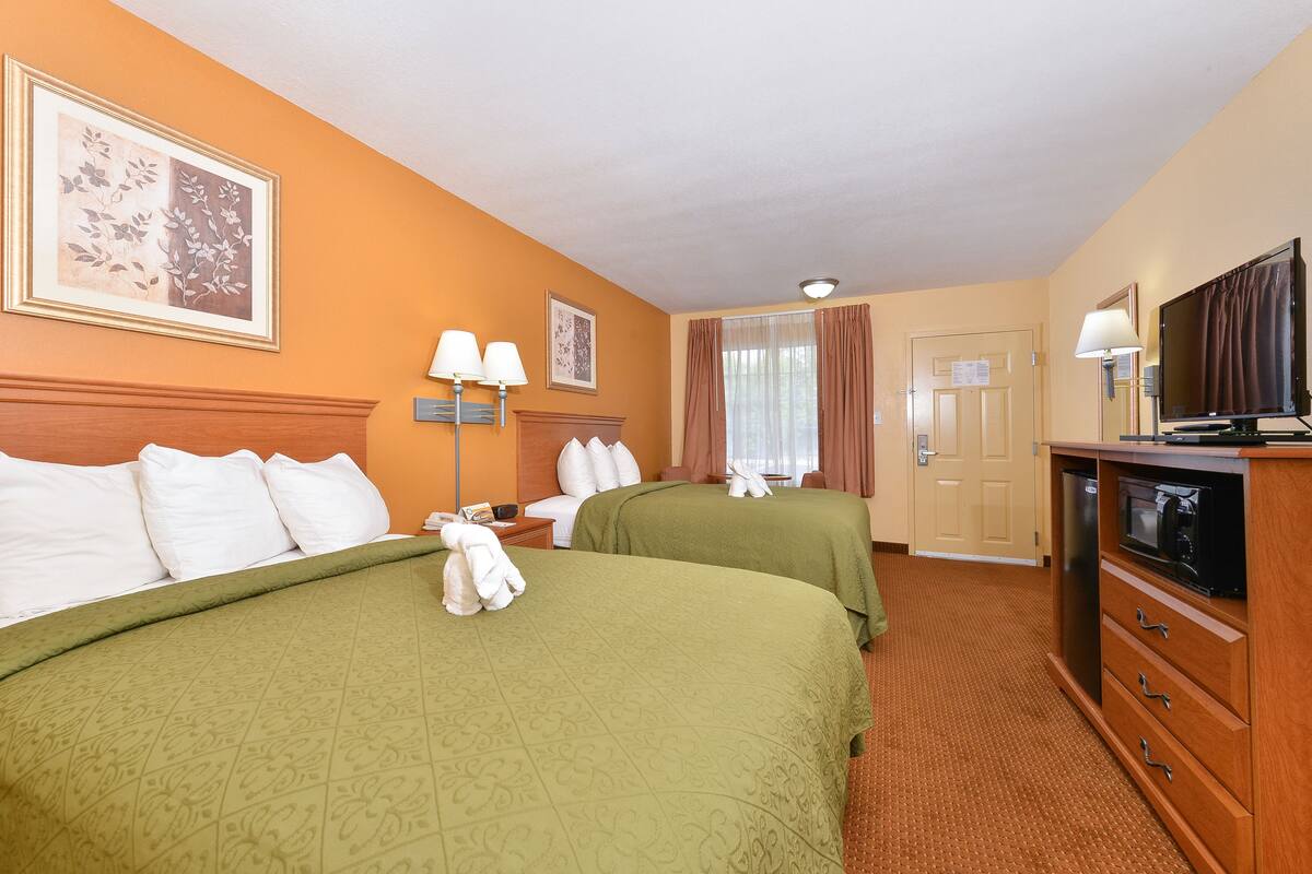 Une chambre d’hôtel avec deux lits, une télévision, un bureau et une fenêtre avec des rideaux.