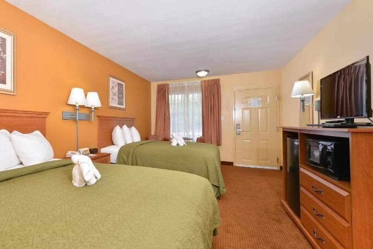 Een hotelkamer met twee bedden, een televisie, een bureau en een raam met gordijnen.