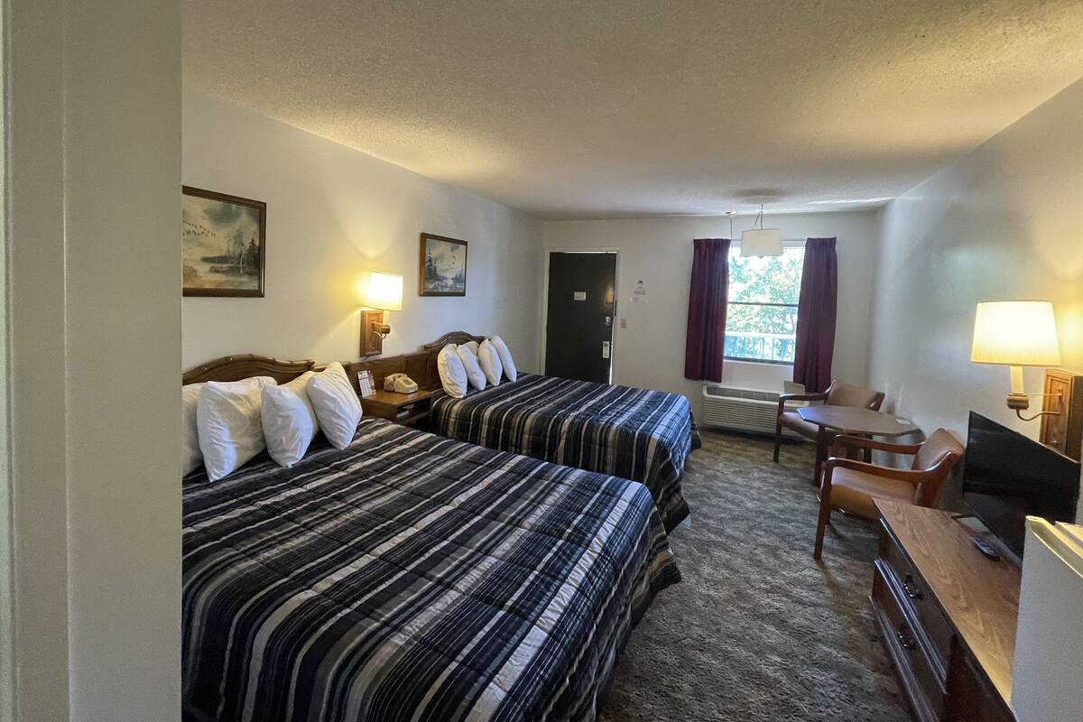 Ett hotellrum med två sängar, ett skrivbord, en stol, en tv och en dörr.