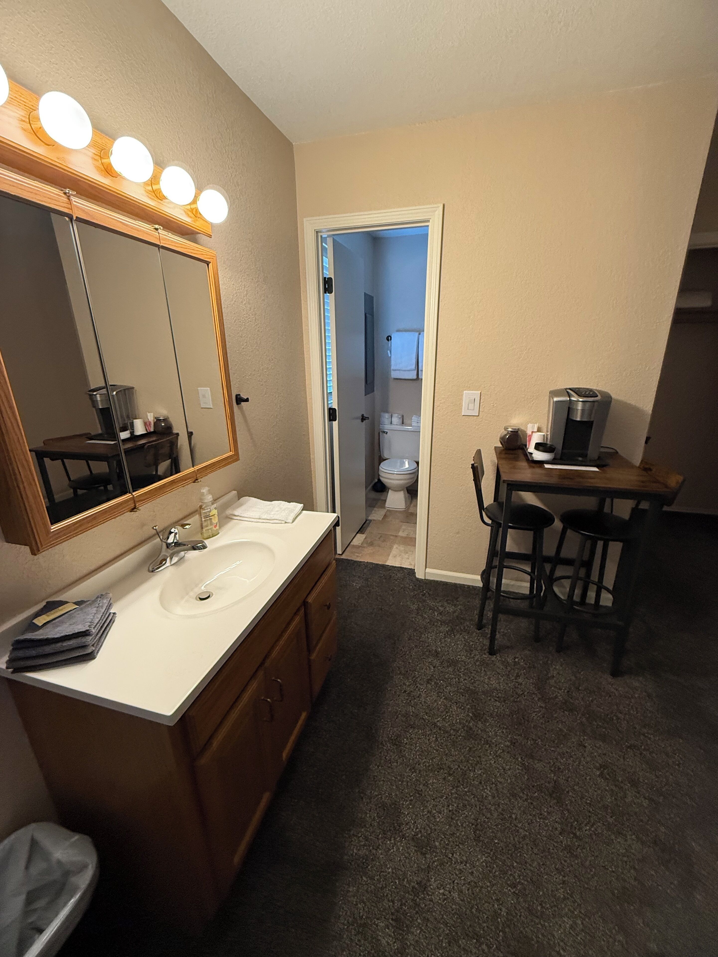 A bathroom with a large mirror, vanity, sink, and a coffee machine on a small table.