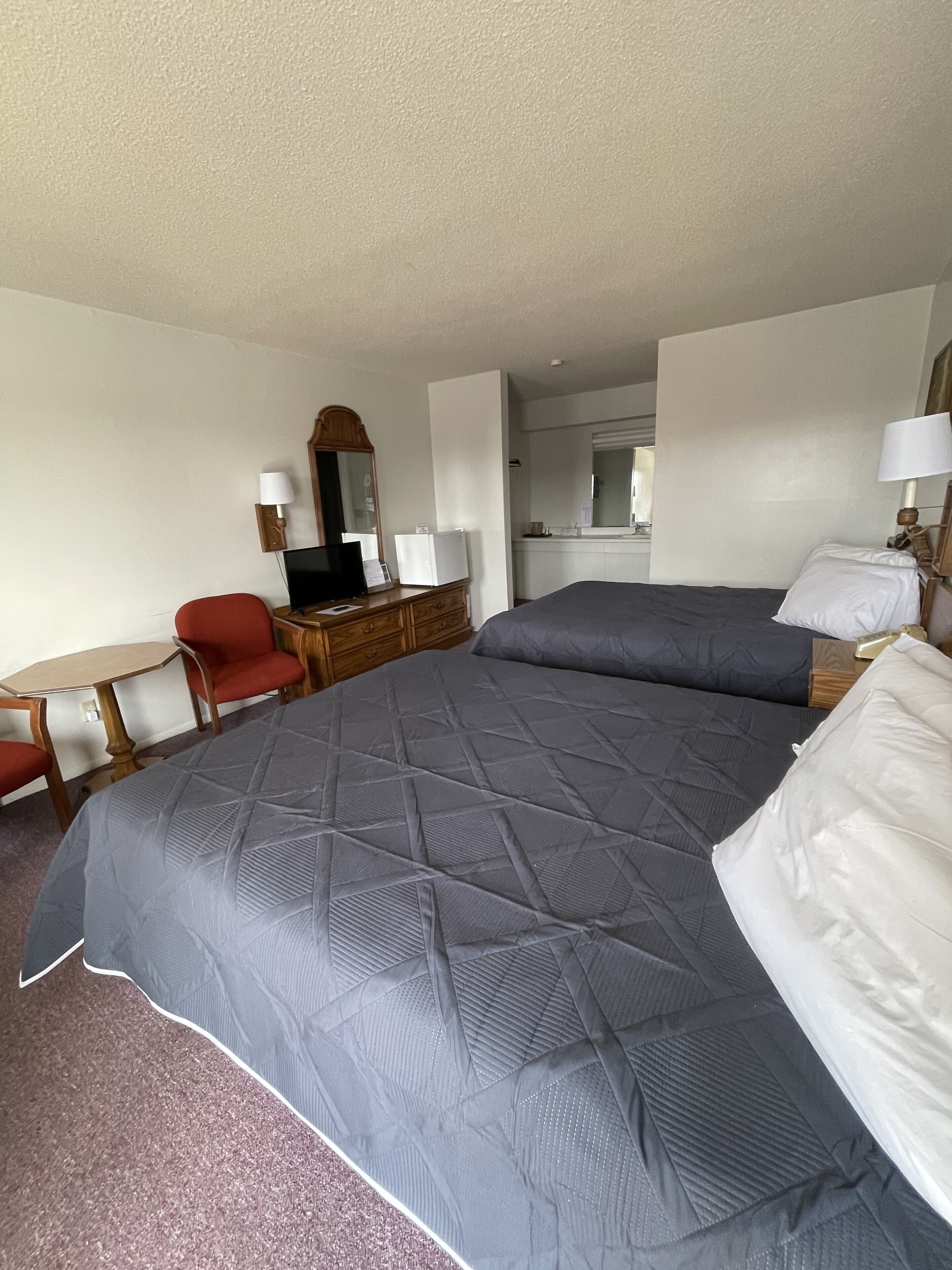 A hotel room with a large bed, a desk with a chair, a dresser, and a mirror.