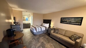 A hotel room with a bed, a sofa, a desk, and a chair. There is a bathroom visible in the background. - The No Wake Inn - Osage Beach (Osage Beach)